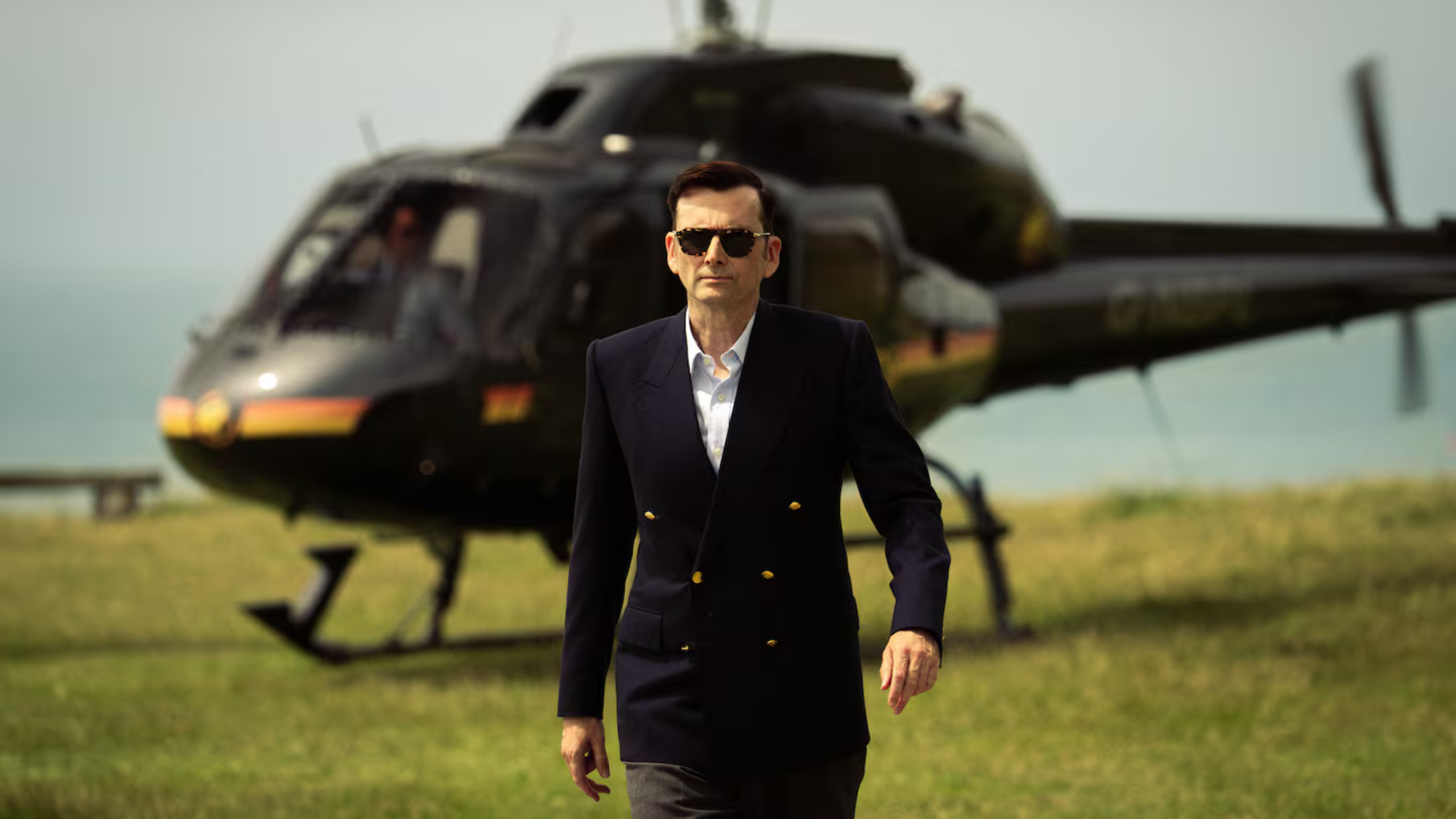 Doctor Who's David Tennant returns of Lord Baddington in Rivals Series 2 (c) Disney+. In navy double breasted suit, Baddington strides determined away from his helicopter